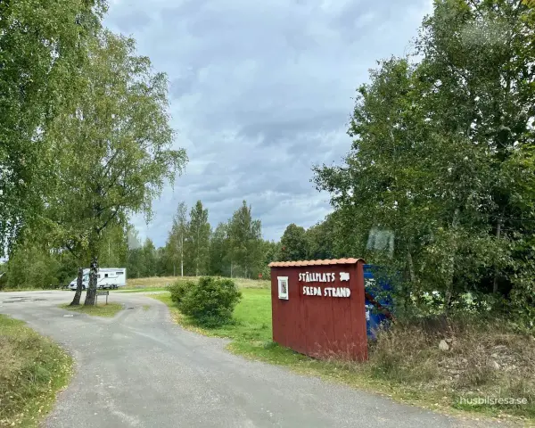 Välkommen till ställplatsen vid Skeda strand. En husbil står parkerad bland träden.