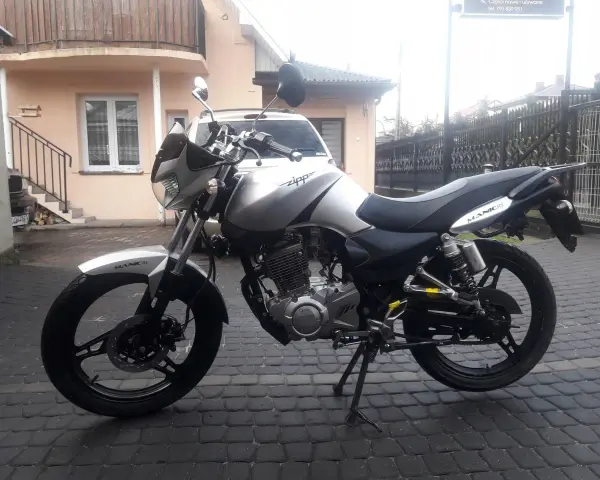 Srebrny Zipp Manic 125 na brukowanym podwórku, gotowy do jazdy.