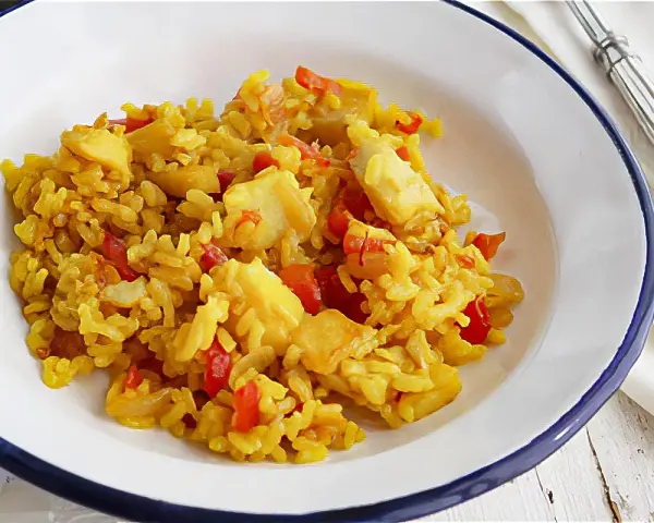 Arroz amarillo con trozos de bacalao y pimientos rojos en un plato blanco.