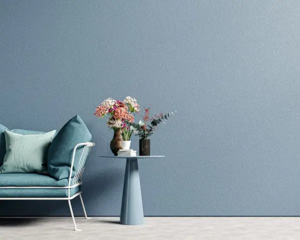 Divano blu e tavolino con fiori su muro azzurro, ispirazione per tecniche di pittura pareti moderne.