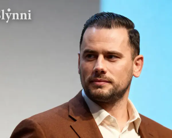 Grzegorz Collins, znany z programów telewizyjnych, w eleganckim brązowym garniturze. Jego wiek jest trudny do określenia, ale prezentuje się dojrzale.