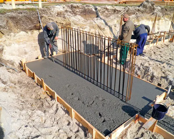 Budowa fundamentów: pracownicy wylewają beton, przygotowując zbrojenie pod przyszły żelbeton.