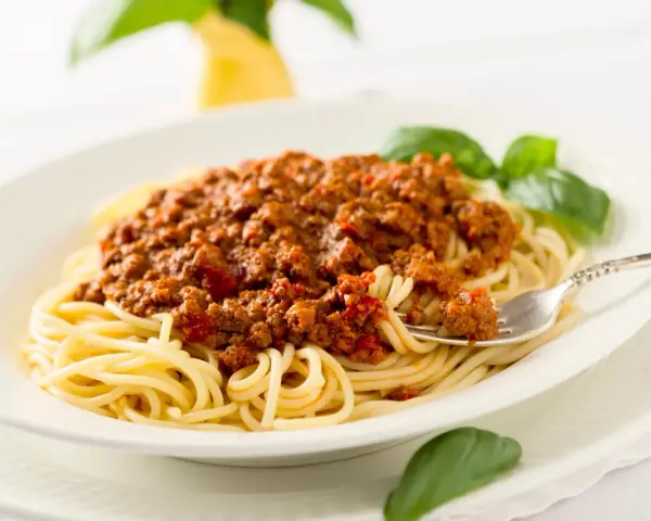Ein Teller Spaghetti mit einer reichhaltigen, traditionell zubereiteten Bolognese-Sauce, garniert mit frischem Basilikum.