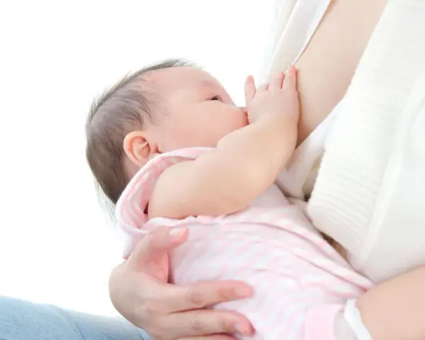 Malutkie dziecko w różowo-białe paski pije mleko mamy. To piękny moment karmienia, kiedy pojawia się nawał pokarmu.