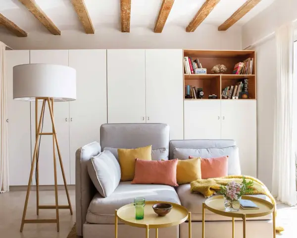 Sofá gris con cojines coloridos, mesa auxiliar amarilla y lámpara de pie. Ideas para decorar piso alquiler low cost con estilo y calidez.