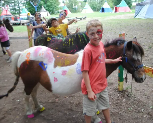 Enfants avec des poneys décorés de peinture, dans un campement avec des tentes.