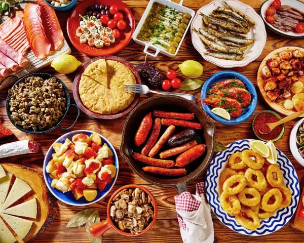 Tapas co to? Obficie zastawiony stół pełen hiszpańskich przekąsek: kiełbaski, krewetki, kalmary, owoce morza, sery, wędliny i tortilla.