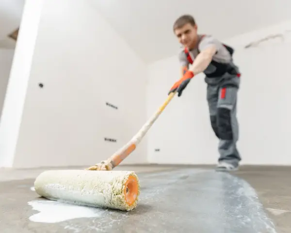 Man målar garagegolv med en roller.