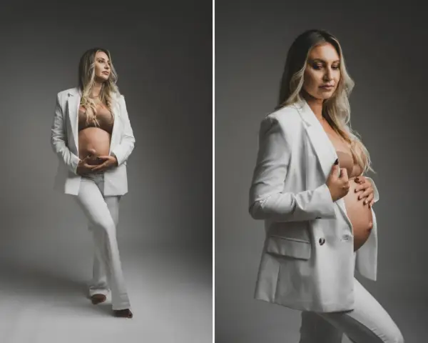 Elegancka kobieta w białym garniturze podczas sesji ciążowej, czule trzymająca się za brzuch.