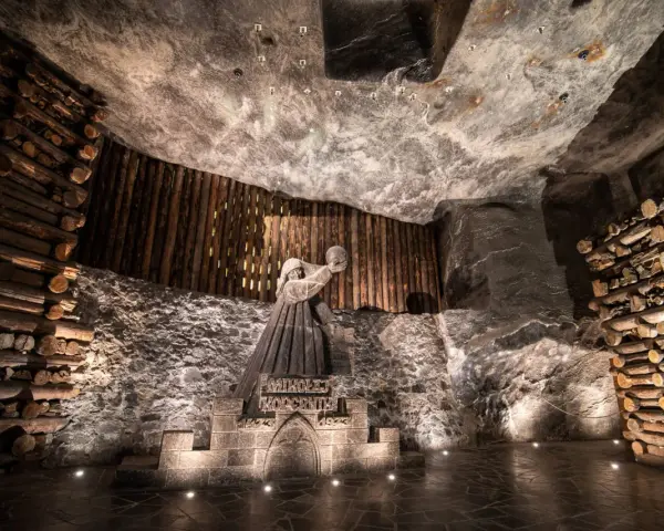 Kopalnia soli Wieliczka ciekawostki: rzeźba górnika Mikołaja Kopernika w solnej komorze, otoczona drewnianymi belkami i solnymi ścianami.