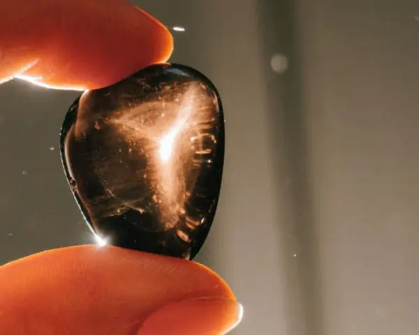 Dedos sostienen una piedra oscura con destellos dorados. ¿Qué pasa si se rompe una piedra energética? Quizás solo se dispersa su luz.