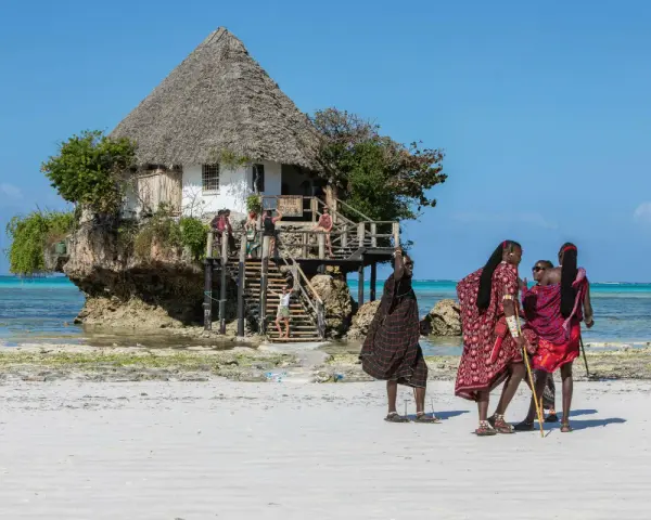 Wspaniały marzec na Zanzibarze. Ludzie w tradycyjnych strojach spacerują po plaży przy restauracji "The Rock" na skale.