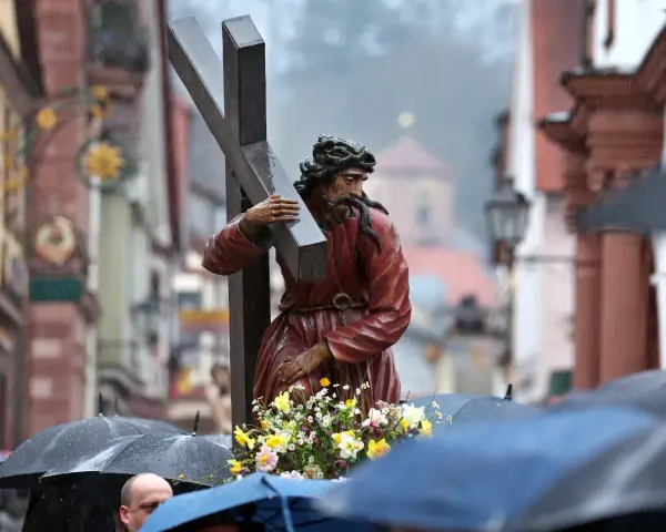 Prozession am Karfreitag: Jesus trägt das Kreuz. Gläubige mit Regenschirmen gedenken.