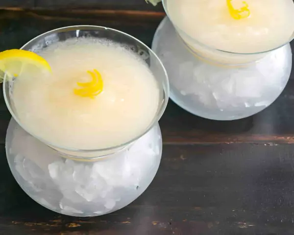 Dos copas de sorbete de limón, una con rodaja de limón y rizo de cáscara, servidas sobre hielo picado.