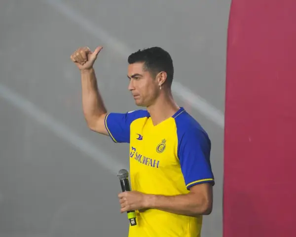 Cristiano Ronaldo w koszulce Al Nassr z mikrofonem, pokazuje kciuk w górę.