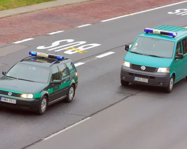 Dwa pojazdy uprzywilejowane Straży Granicznej, zielony kombi i turkusowy van, jadą drogą.