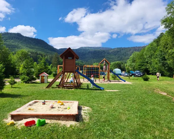 Plac zabaw dla dzieci na terenie radków camping. Piaskownica, zjeżdżalnie i drabinki w otoczeniu zieleni i gór.