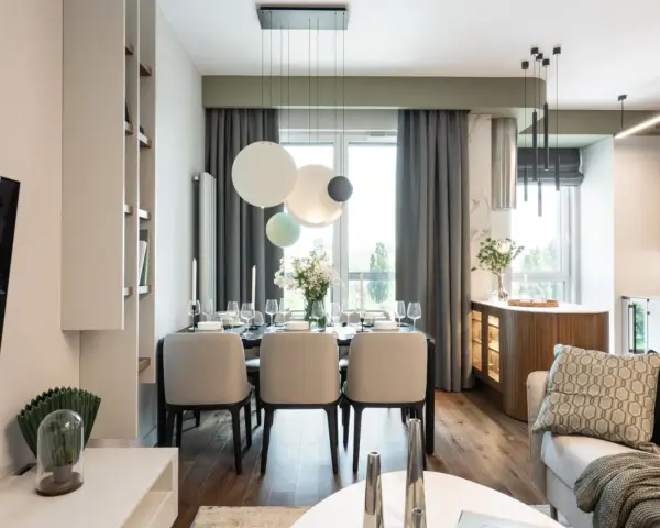 Elegancka jadalnia z nowoczesnym stołem i krzesłami. W tle kuchnia z drewnianymi elementami i subtelnym akcentem w kolorze pistacjowym.