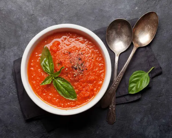 Eine Schüssel mit leckerer, italienischer Tomatensauce, garniert mit Basilikum und Pfeffer. Daneben liegen zwei Löffel.
