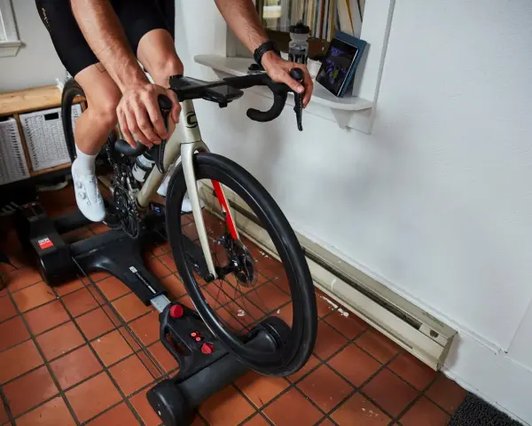 Cyclist on bike rollers, a dynamic alternative to a trainer, rides indoors while watching a tablet.