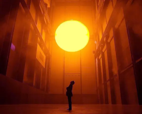 Une personne contemple un soleil artificiel dans l'installation "The Weather Project" d'Olafur Eliasson, baignant l'espace d'une lumière orangée intense.