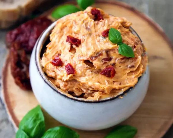 Cremige Tomatenbutter, garniert mit Basilikum und getrockneten Tomatenstücken. Perfekt für ein einfaches Tomatenbutter Rezept.
