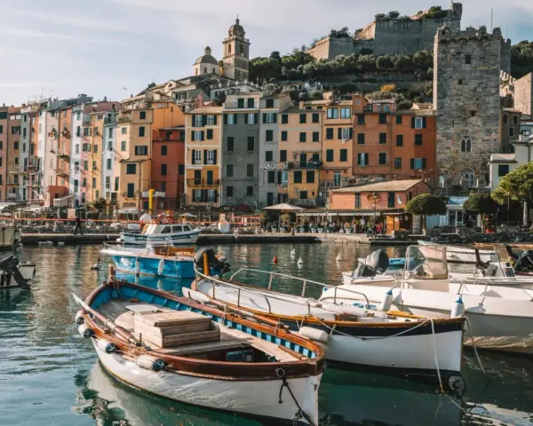 Boats bob in the harbor of a colorful Italian Riviera town, with ancient castles overlooking the vibrant buildings.