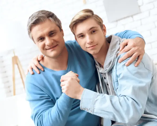 Ojciec obejmuje syna, wspierając go w ważnych życiowych rozmowach.