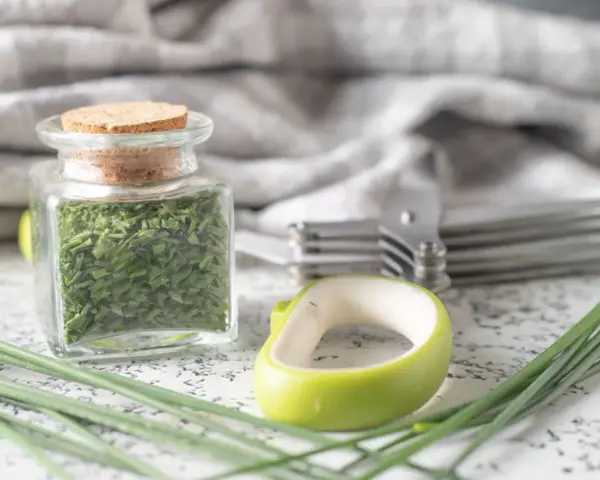 A jar filled with dried chives, showcasing how to dry chives for long-term storage. Fresh chives and kitchen tools are nearby.