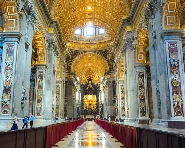 Interior of a grand basilica in Rome, with ornate golden ceilings, marble columns, and a long aisle lined with red velvet.