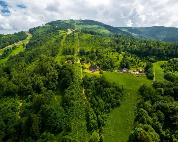 Widok z lotu ptaka na zielone wzgórza Beskidu Śląskiego ze szlakami i domkami.