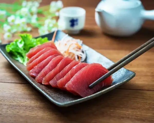 Pyszne japońskie ryby, świeże sashimi z tuńczyka, podane z sałatką i sosami. Pałeczki gotowe do degustacji.