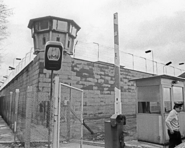 Wachturm und Grenzbefestigung der deutschen demokratischen Republik. Ein Wachmann steht neben einer Schranke und einem Kontrollhäuschen.