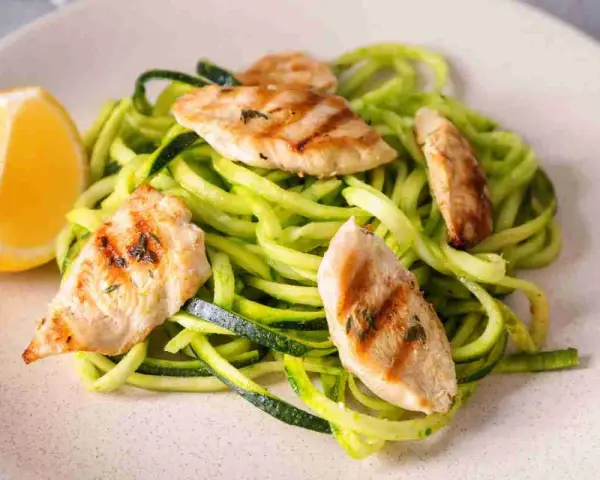 Spaghetti di zucchine con straccetti di pollo grigliato e una fetta di limone.