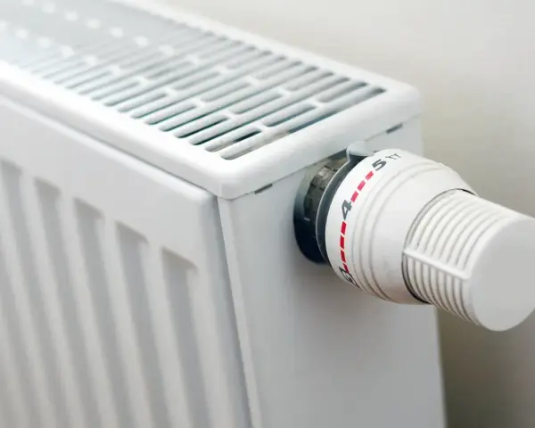 Biały grzejnik z termostatem. Różne rodzaje grzejników oferują różne sposoby regulacji temperatury.
