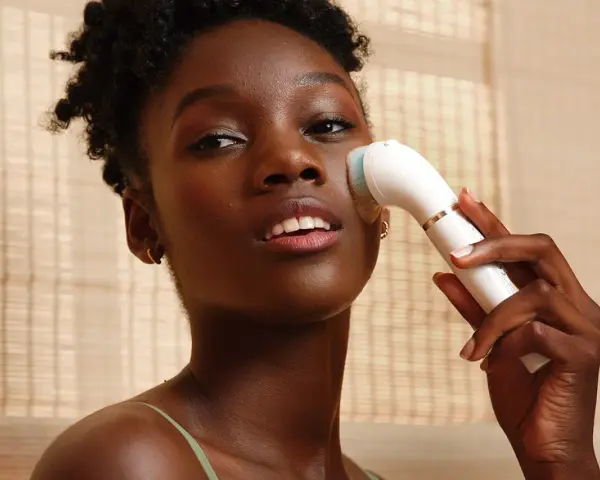 Donna con pelle scura usa un dispositivo per un trattamento esfoliante viso, per una pelle luminosa e pulita.
