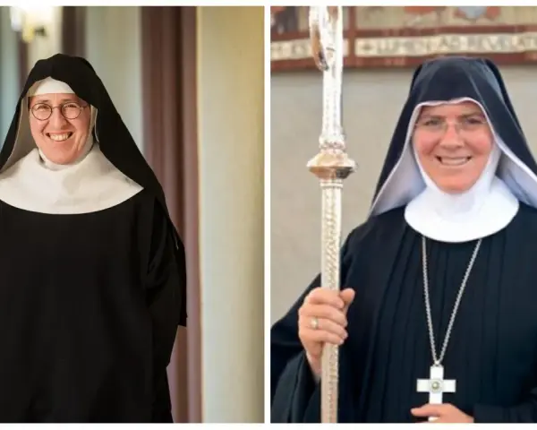 Two smiling nuns in traditional black habits and white wimples. This is what Catholic monks wear, along with a cross necklace and a staff.