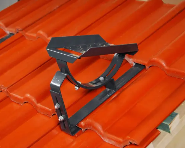 Metalowe stopnie kominiarskie zamontowane na pomarańczowej dachówce. Zapewniają bezpieczeństwo podczas prac na dachu.