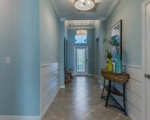Un couloir lumineux avec une peinture de couloir 2 couleurs : bleu ciel et blanc. Un banc, une console avec des vases et une porte vitrée ornent cet espace accueillant.