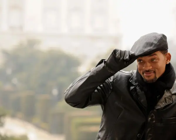 Will Smith, con un berretto uomo, giacca di pelle e sciarpa, saluta con un sorriso.
