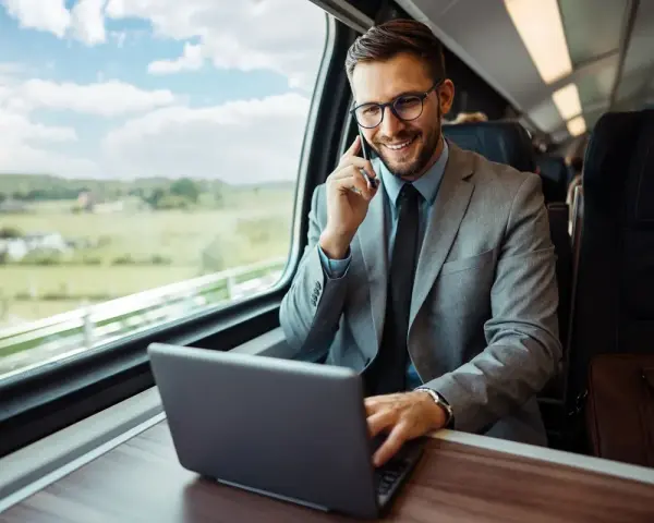 Biznesmen w garniturze rozmawia przez telefon i pracuje na laptopie w pociągu.
