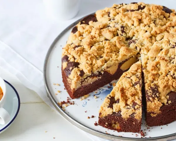 Ein saftiger Apfel Schokoladenkuchen mit knuspriger Streuseldecke, daneben eine Tasse Kaffee.