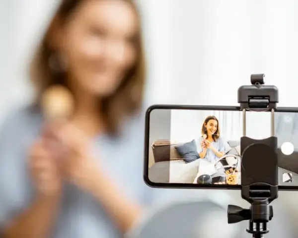 Kobieta nagrywa filmik telefonem komórkowym, trzymając pędzel do makijażu.