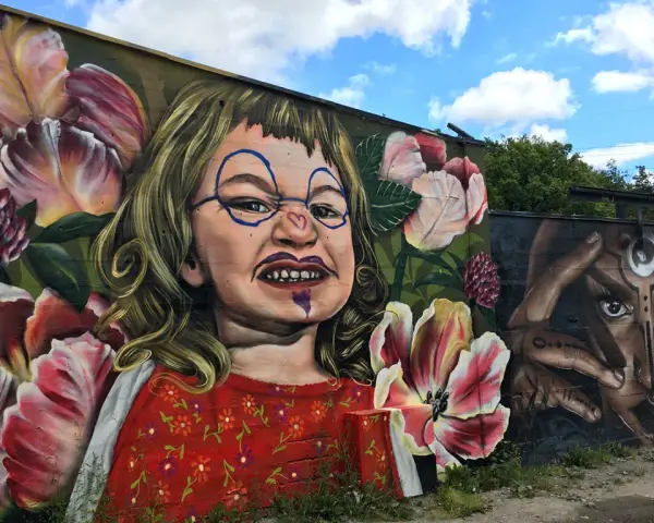 En väggmålning med en busig flicka omgiven av blommor ger graffiti inspiration. Bredvid syns ett mystiskt ansikte med händer.