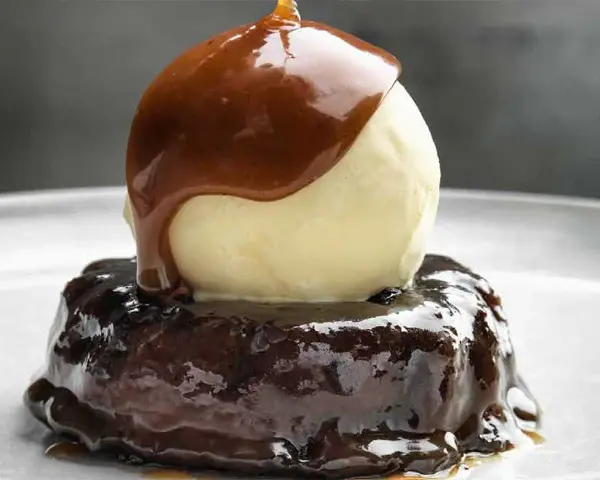 En läcker sticky toffee pudding med en kula vaniljglass och varm kolasås som rinner över.