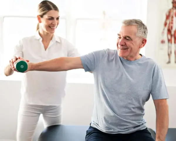 Mann hebt Hantel unter Anleitung einer Therapeutin. Physiotherapie nach Bobath hilft bei der Rehabilitation.