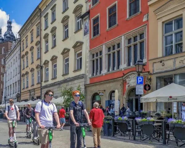 Młodzi ludzie na hulajnogach w Krakowie, idealne na city break. W tle Sukiennice i Kościół Mariacki.