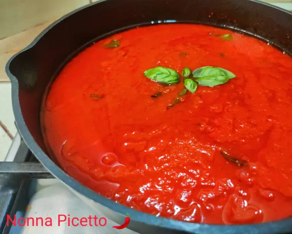 Sugo al pomodoro fresco e profumato, con foglie di basilico che galleggiano in una padella di ghisa.