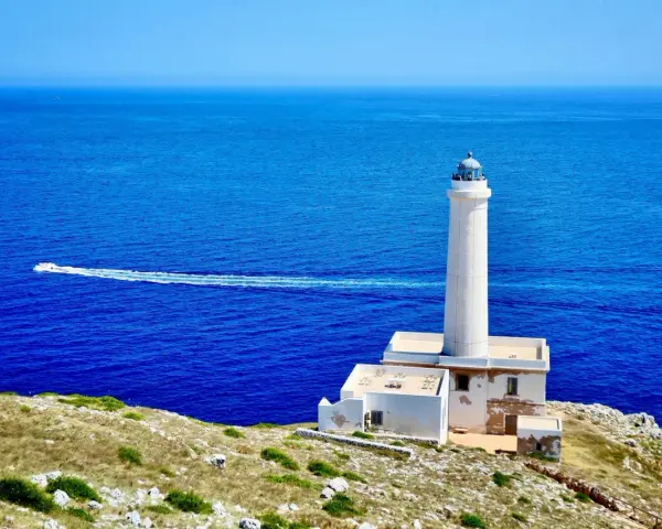 Faro di Punta Palascìa, uno dei luoghi da vedere a Otranto, con il mare blu e una barca in lontananza.