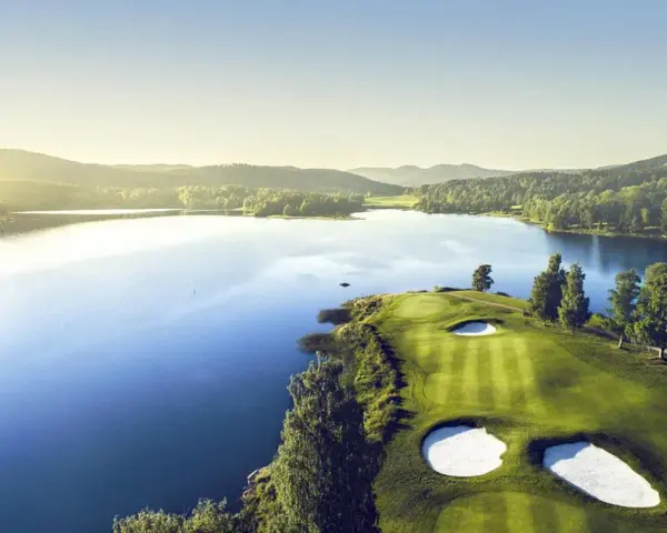 Vacker golfbana vid en sjö, perfekt för norsk golf. Grönskande kullar och solnedgång.